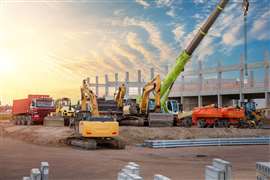 Many different multiclored colorful heavy industrial machinery equipment at construction site parking area against warehouse building city infrastructure development.